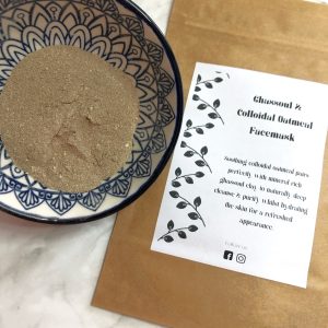 Bowl containing ghassoul facemask next to facemask sachet