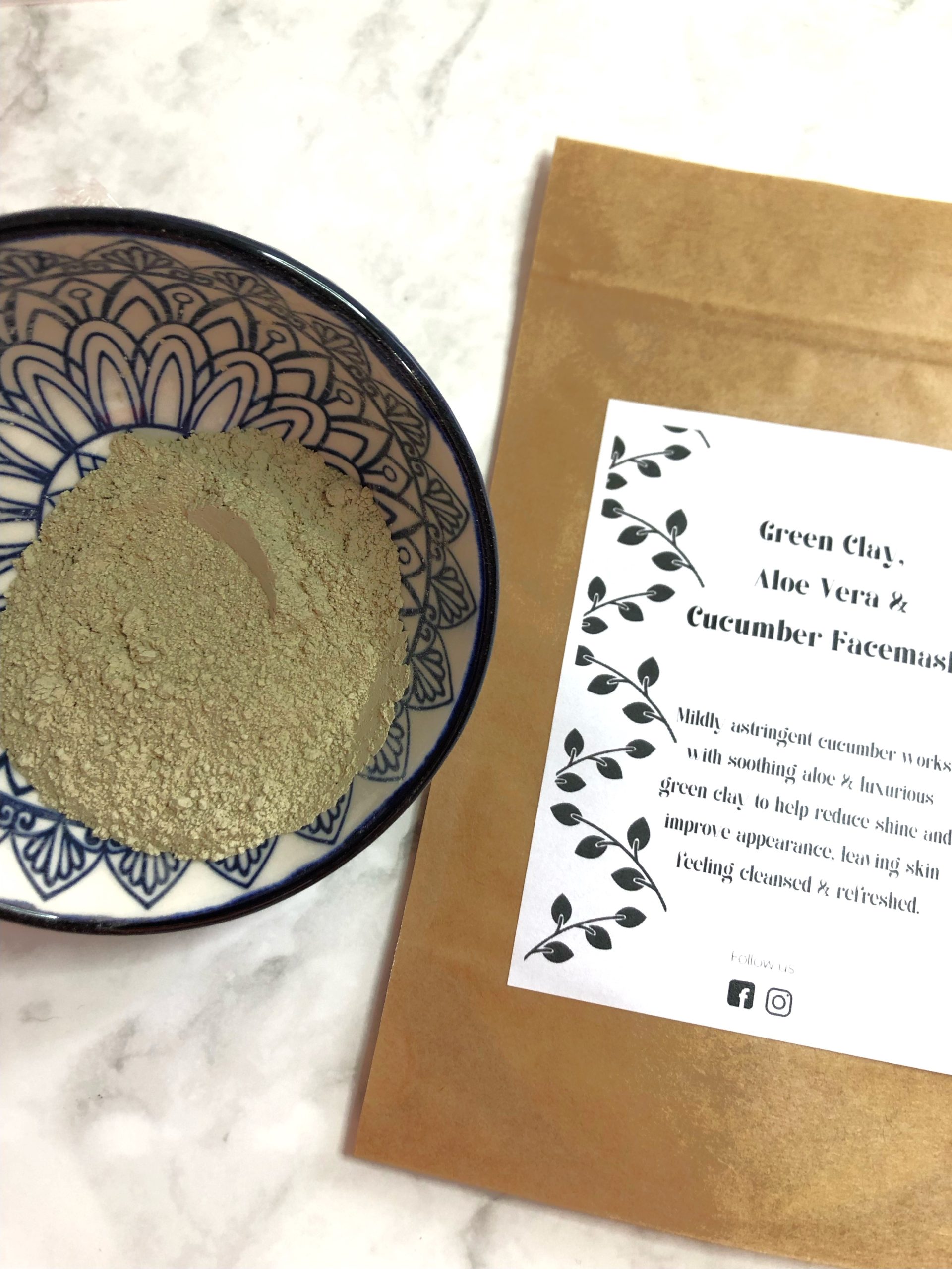 Bowl containing green clay face mask next to face mask sachet
